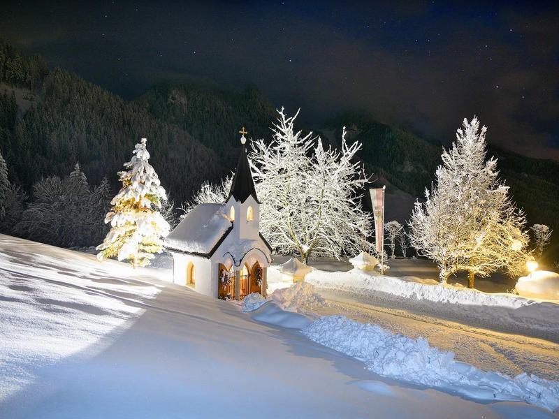 Paysage hivernal avec maison illuminée, arbres enneigés et collines en arrière-plan la nuit