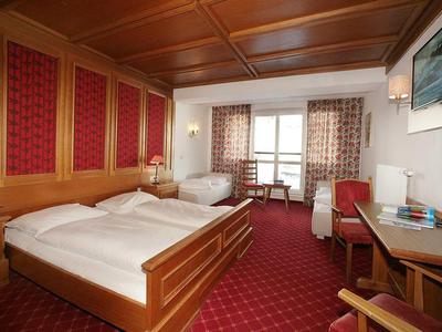 Pohodlný hotelový pokoj s manželskou a jednolůžkovou postelí, dřevěným nábytkem a balkonem s výhledem.