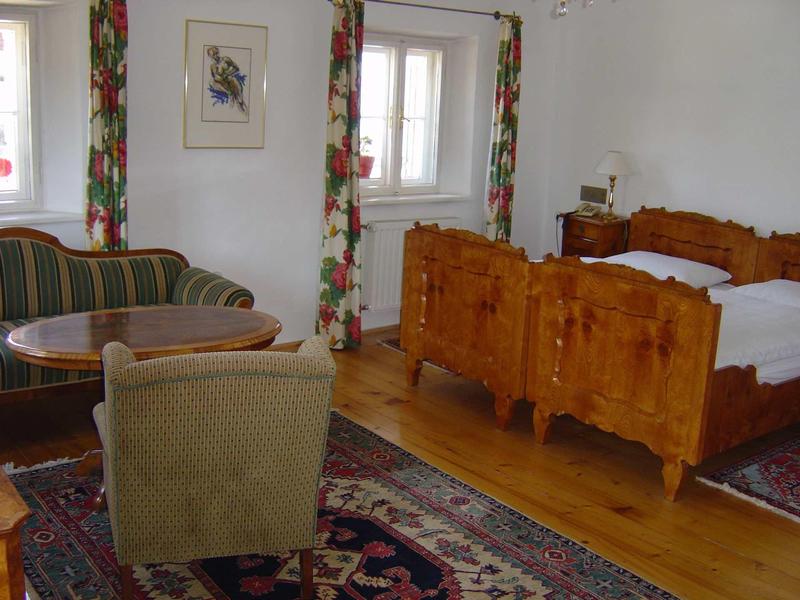 Pohodlný hotelový pokoj s dřevěným nábytkem, pohovkou, křeslem a kobercem před dvěma postelemi.