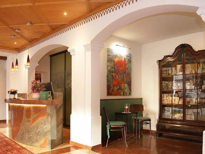 Hotelová recepce s kamenným pultem, zelenými židlemi a tmavou dřevěnou vitrínou.