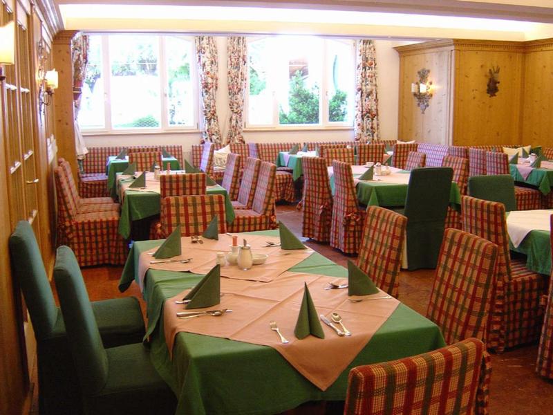 Příjemná jídelna se zelenými stolky a kostkovanými židlemi.