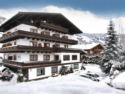 Hôtel enneigé à la montagne avec des fleurs sur le balcon sous un ciel bleu.