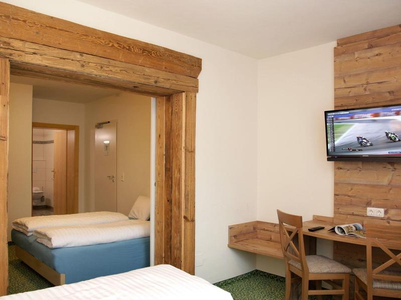 Eenvoudige hotelkamer met twee eenpersoonsbedden, houten meubels en een aan de muur gemonteerde tv.