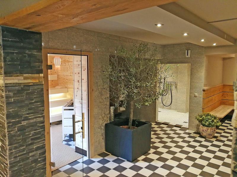 Hotelgang met zwart-witte tegelvloer, een boom in pot, stenen muren en houten details.