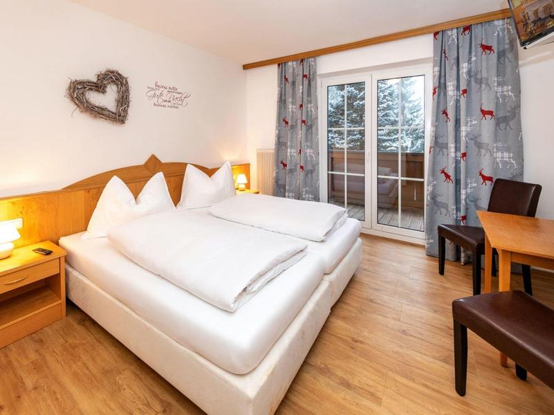 Chambre d'hôtel lumineuse avec lit double, meubles en bois et balcon avec vue sur les arbres.