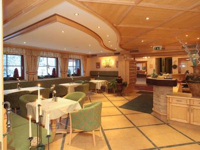 Großer, hell beleuchteter Gastraum mit Holztäfelung, grünen Sesseln und gedeckten Tischen.