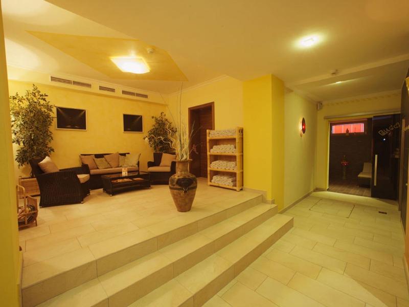 Flur mit Treppen, gelben Wänden und Sitzbereich mit Sofas und Pflanzen in warmem Licht.