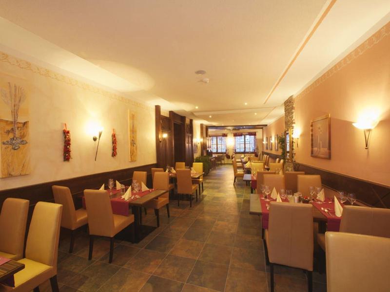 Hell beleuchteter Restaurantraum mit beigen Wänden, Stühlen und Tischen, dekoriert mit Wandbildern.