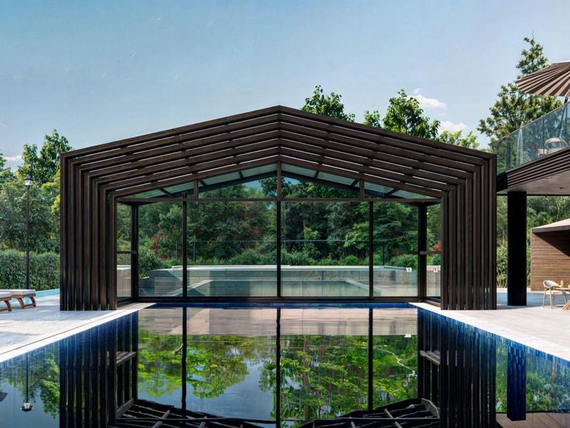 Moderner Außenpool mit Glasüberdachung, Holzstruktur und sonnigen Liegestühlen, umgeben von Grün.