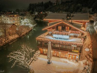 Night view of a lit hotel beside a river with snow-covered trees.