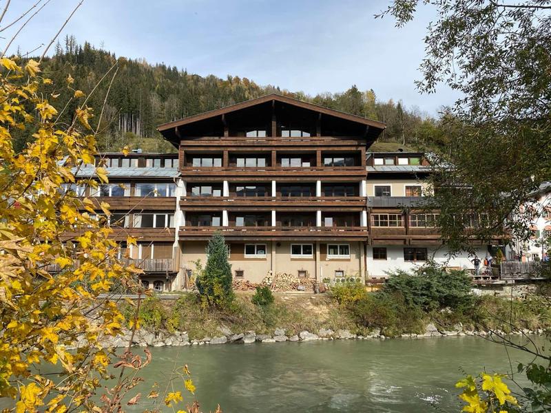 Large chalet hotel by the river with autumn foliage in the foreground.