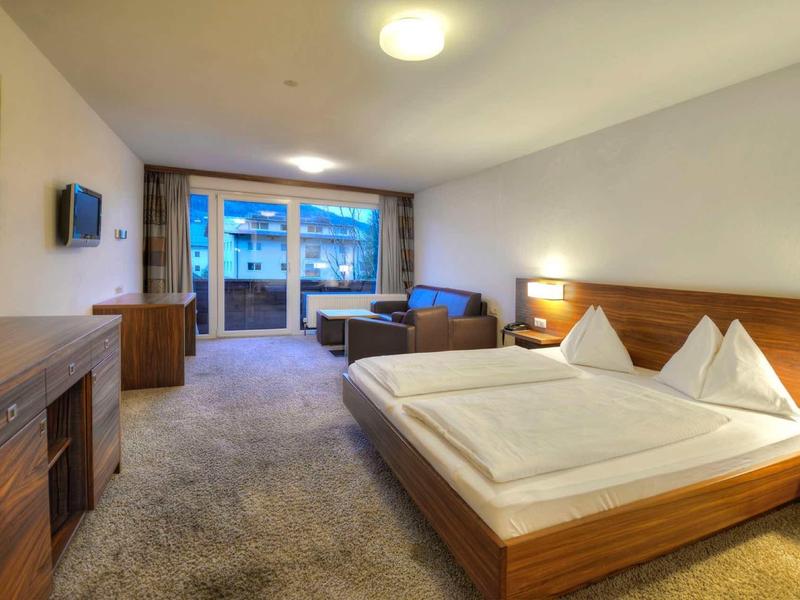 Spacious hotel room with double bed, seating area, and large balcony with panoramic view.
