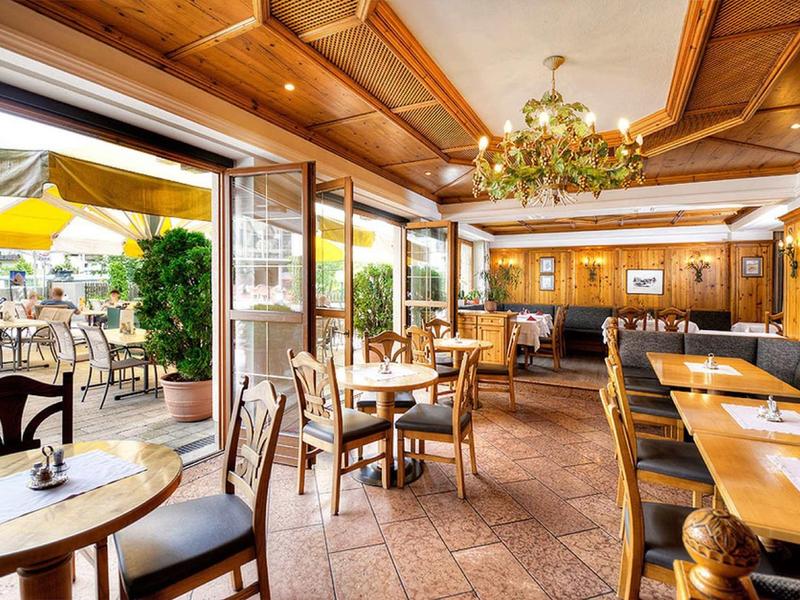 Bright restaurant with wooden furniture, chandelier, and view of a terrace with umbrellas.