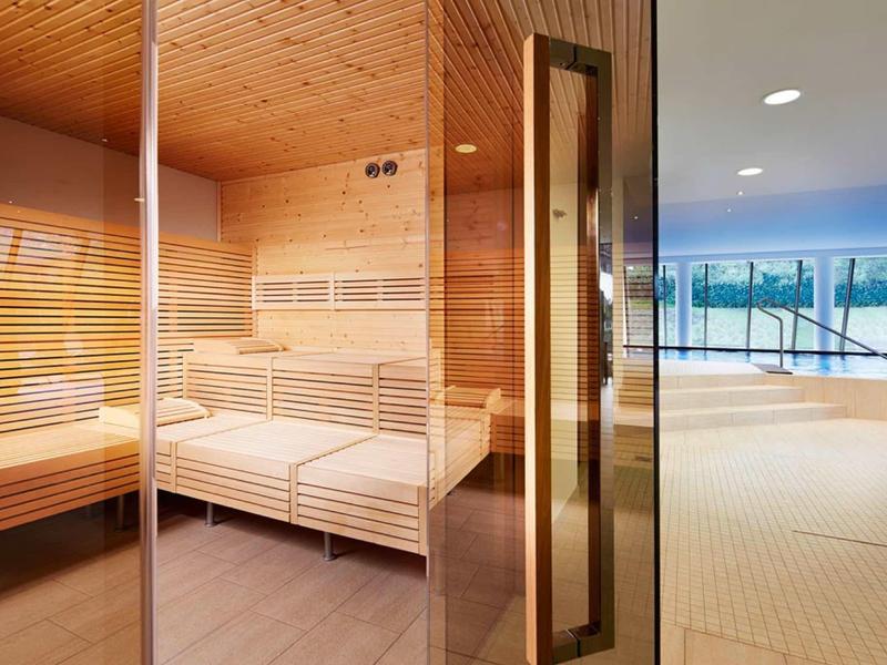 Sauna con pareti e panchine in legno accanto a una grande finestra che dà su una piscina.
