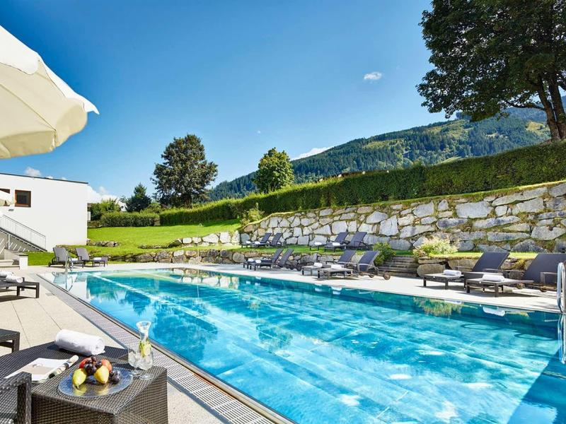 Piscina limpida con lettini e ombrellone in un ambiente montano verde e soleggiato.