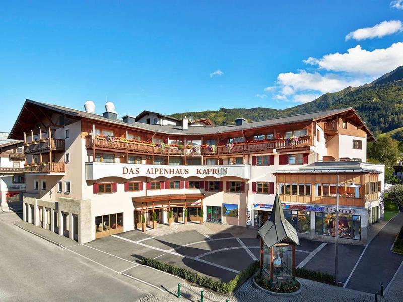 Grande edificio dell'hotel con balconi davanti a montagne boscose sotto un cielo blu.
