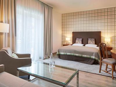 Modern hotelkamer met tweepersoonsbed, zithoek en grote ramen met gordijnen