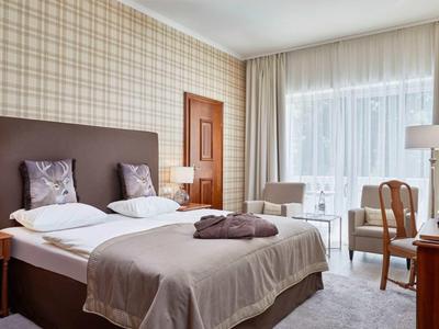 Gezellige hotelkamer met tweepersoonsbed, fauteuils en bureau, helder en modern ingericht.