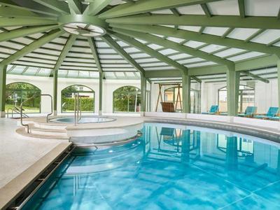 Overdekt zwembad met grote ramen, ligstoelen en groene architectuur.