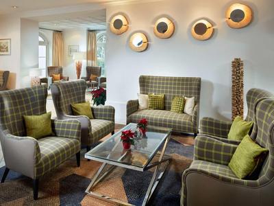 Gezellig zitgedeelte met geruite fauteuils, bank en glazen salontafel in hotel lounge.