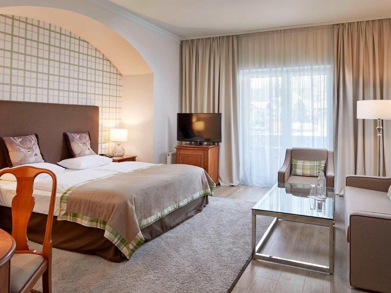 Moderne hotelkamer met tweepersoonsbed, zithoek, tv en balkon met gordijnen.