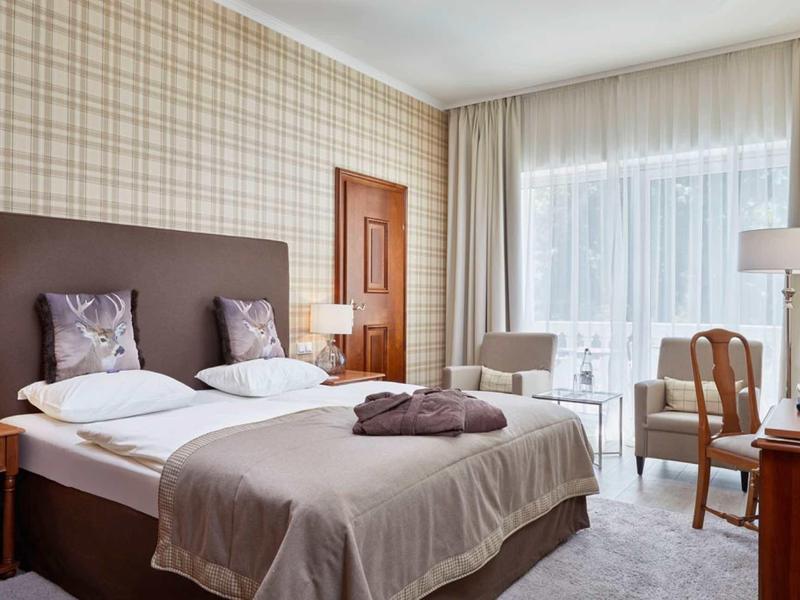 Gezellige hotelkamer met tweepersoonsbed, fauteuils en bureau, helder en modern ingericht.