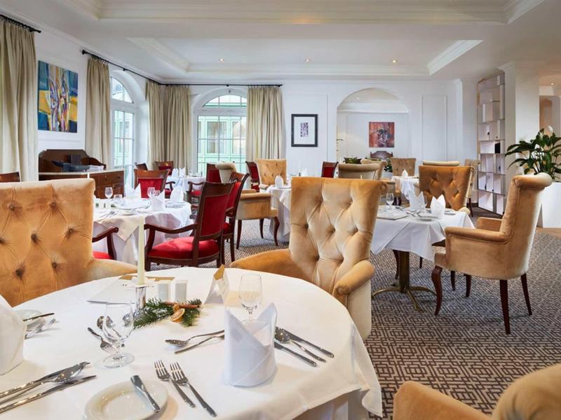 Elegant hotelrestaurant met witte tafelkleden, comfortabele gestoffeerde stoelen en natuurlijk licht.