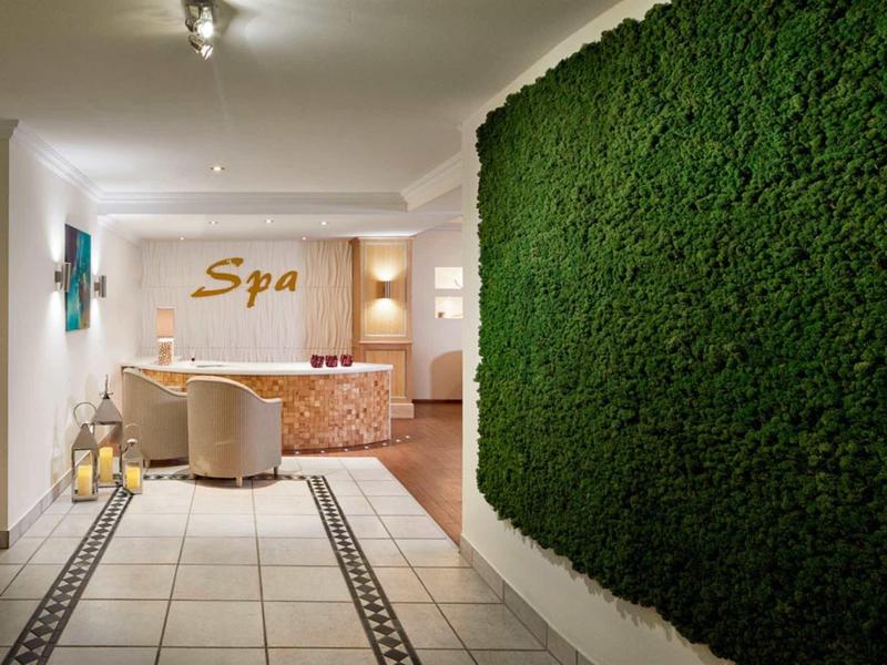 Gang met groene plantenmuur en uitnodigende spa-ingang met stoelen en tafel.