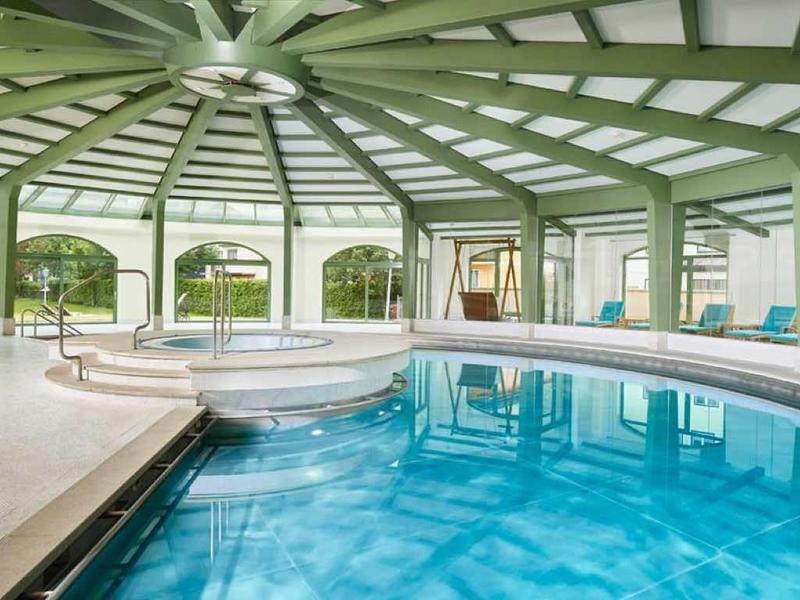 Overdekt zwembad met grote ramen, ligstoelen en groene architectuur.