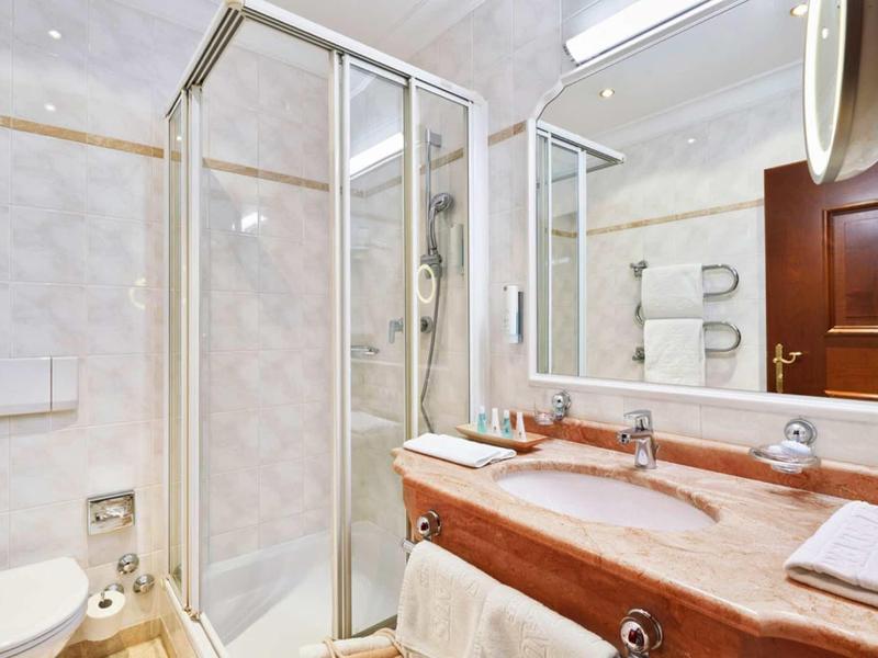 Compacte badkamer met douchecabine, wastafel met grote spiegel en handdoeken.