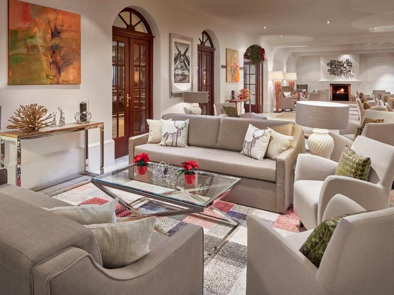 Een lichte, gezellige woonkamer met banken, fauteuils en een glazen tafel in een hotel.