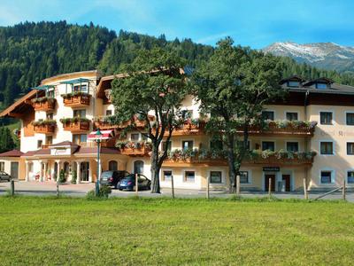 Großes Hotelgebäude vor bewaldeten Hügeln mit grüner Wiese im Vordergrund.