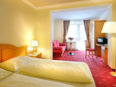 Hotelzimmer mit zwei Einzelbetten, Sesseln und Fernseher in einem angrenzenden Wohnzimmer