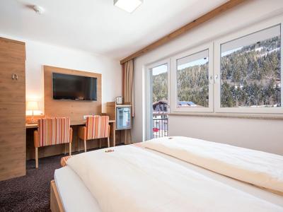 Helles Hotelzimmer mit Bett, Fernseher, Schreibtisch und Aussicht auf schneebedeckte Berge.