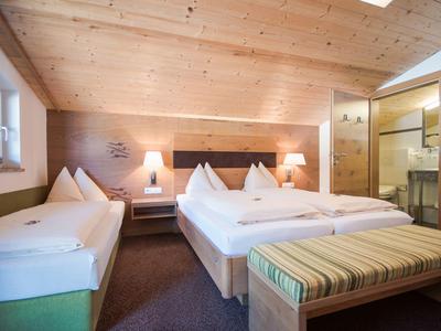 Modernes Hotelzimmer mit Holzwänden, drei Betten und Bad mit Glasdusche.