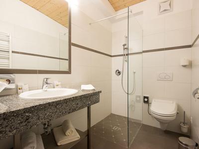 Modernes Badezimmer mit Granitwaschbecken, WC und begehbarer Dusche in warmem Holz- und Weißton.