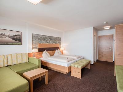 Modernes Hotelzimmer mit Doppelbett, grünem Sofa und schlichtem Dekor.