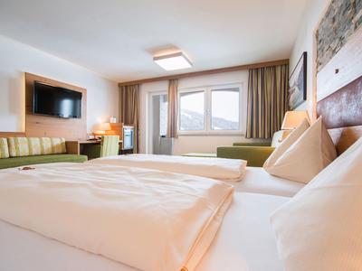 Helles Hotelzimmer mit großen Fenstern, Doppelbett, Sofa und modernem Fernseher.