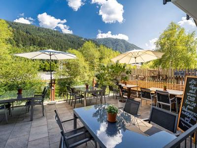 Terrasse mit Sonnenschirmen und Tischen vor grünen Hügeln unter blauem Himmel
