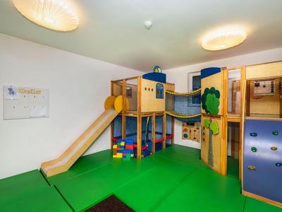 Kinderspielbereich mit Klettergerüst, Rutsche und weichen grünen Bodenmatten.