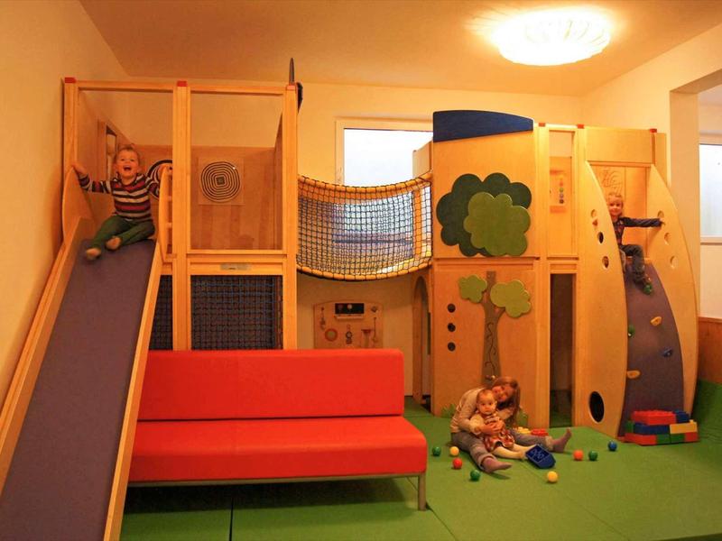 Wewnętrzny plac zabaw z drabinką, zjeżdżalnią i ławką przy ciepłym oświetleniu.