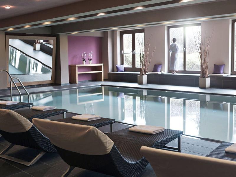 Piscina cubierta con sillones y grandes ventanas que dejan entrar luz natural.