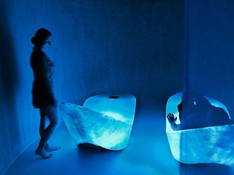 Silueta de una mujer en un interior de hotel azul con muebles futuristas y ambiente tenue.