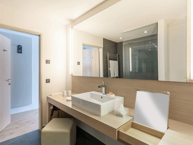 Espejo de baño luminoso con lavabo y estante de madera, comodidad moderna en hotel.