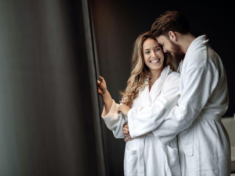 Pareja feliz con batas blancas junto a la ventana en una habitación de hotel.