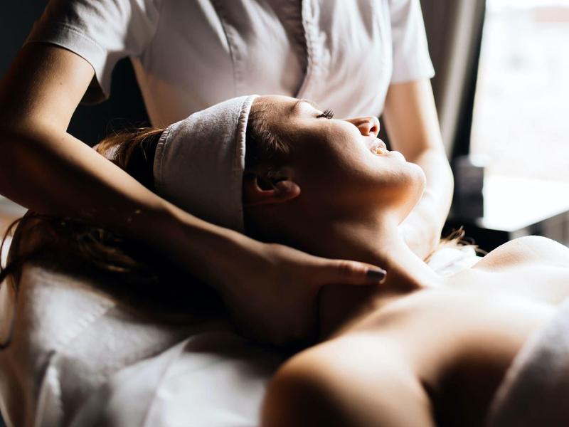 Mujer relajada recibiendo un masaje de cuello en un spa con luz tenue.