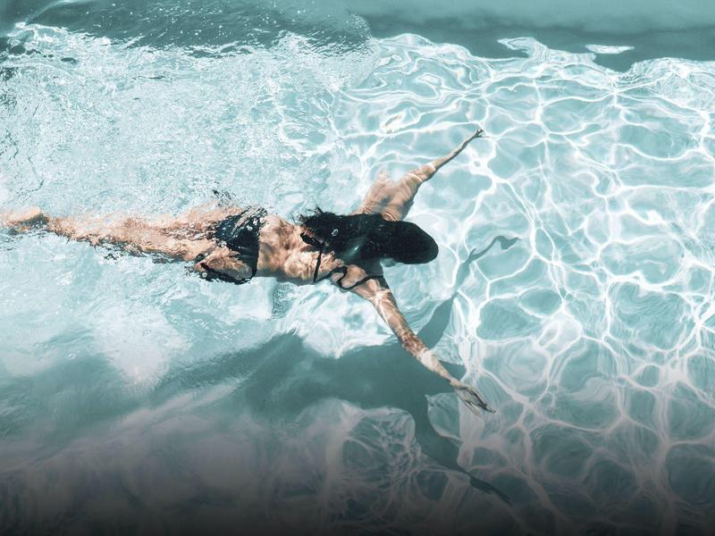 Mujer nada relajada en agua clara de piscina azul con reflejos de luz solar.