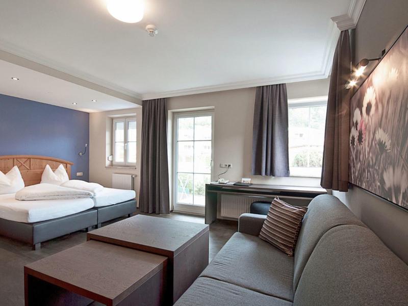 Escena moderna de habitación de hotel con cama doble, sofá y ventana grande con cortinas.