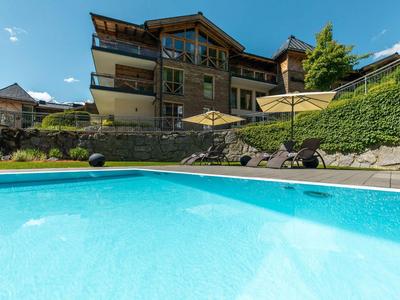 Outdoor pool with clear blue water in front of a chalet-style hotel building on a sunny day.