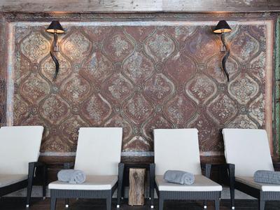 Four white cushioned chairs with towels under iron wall lights on patterned wall.